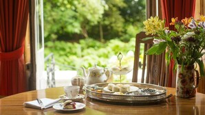 Une table dressée avec un plateau de pâtisseries, une théière, des tasses et un vase de fleurs.