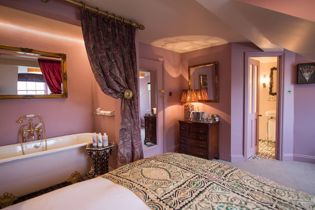 A bedroom with a large bed, a bathtub, a dresser, and a mirror.