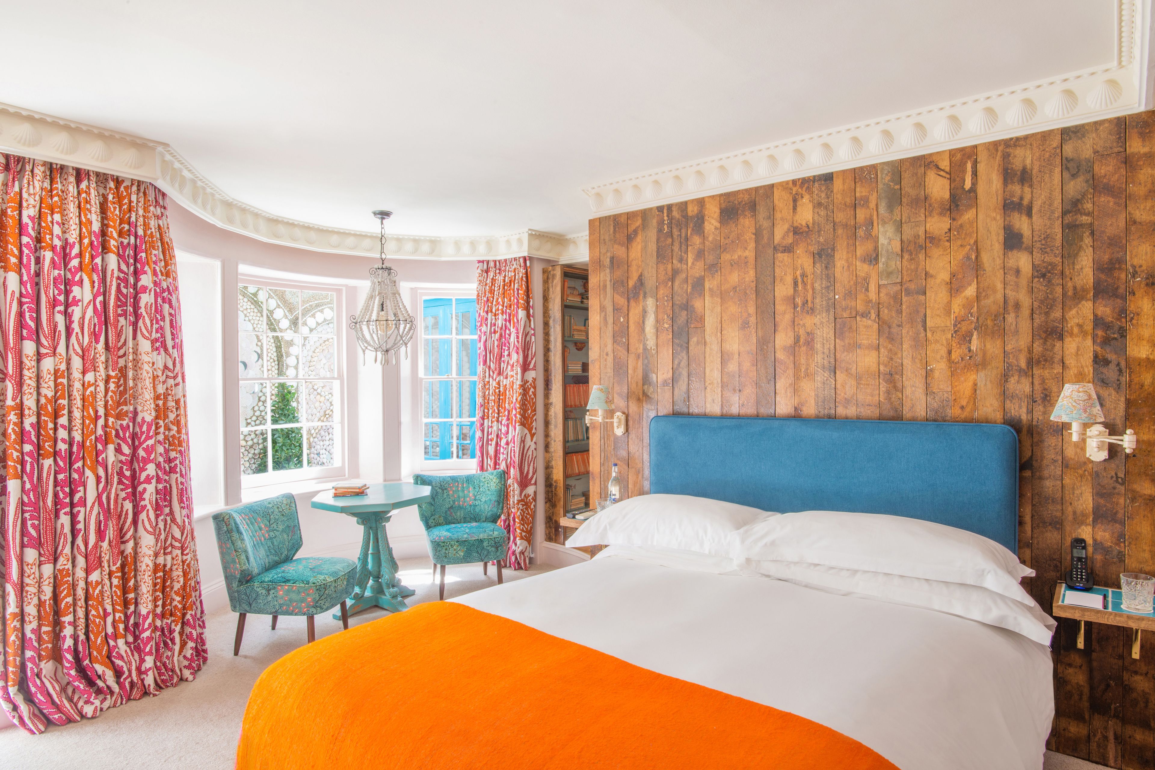 Habitación de hotel con una cama grande, cabecera de madera, una mesita con sillas y vistas al exterior a través de una ventana.
