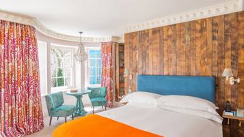 Habitación de hotel con una cama grande, cabecera de madera, una mesita con sillas y vistas al exterior a través de una ventana.