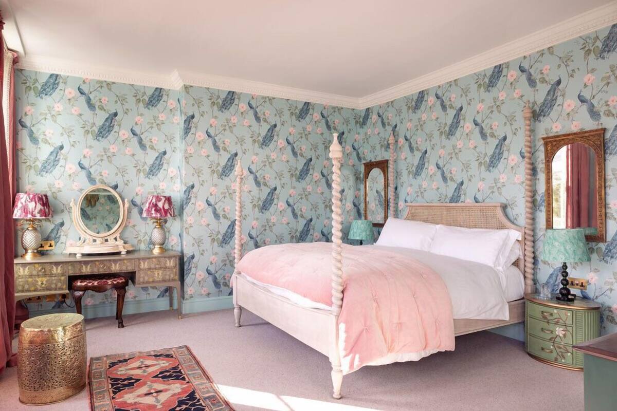 A bedroom with a four-poster bed, a dresser with a mirror, and a nightstand with a lamp.