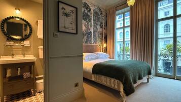 Una habitación de hotel con baño, una cama, un ventanal grande con cortinas y un candelabro.