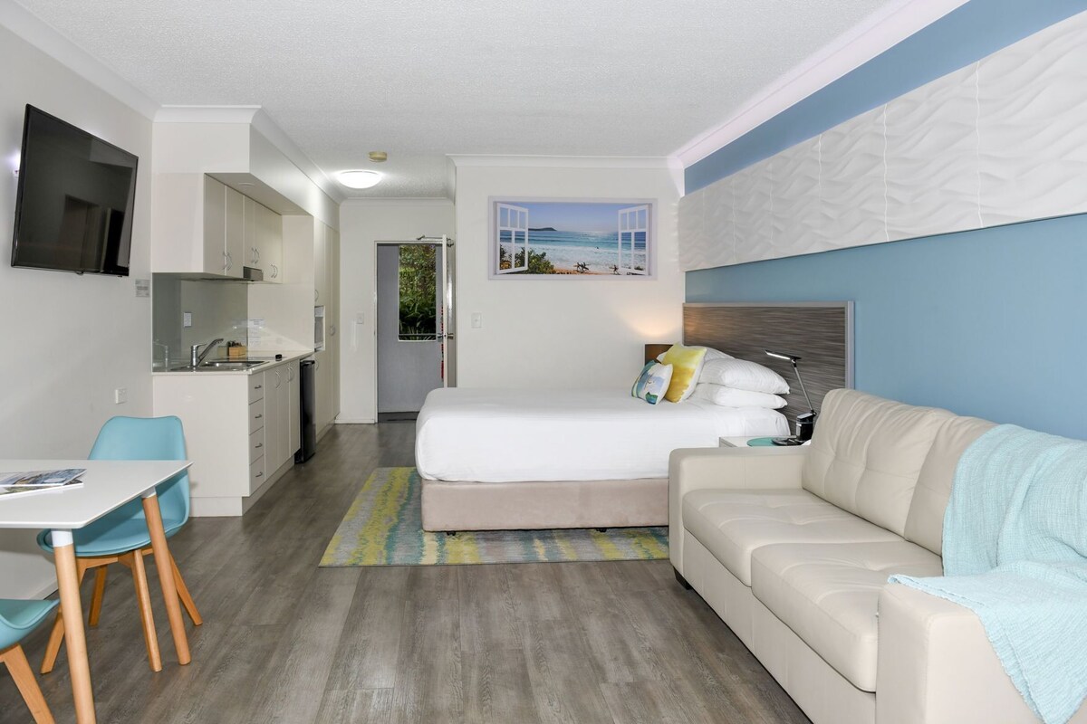Una habitación de hotel compacta con cama, sofá, mesa de comedor y kitchenette.