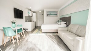 Una habitación compacta con kitchenette, cama, sofá y zona de comedor con sillas.