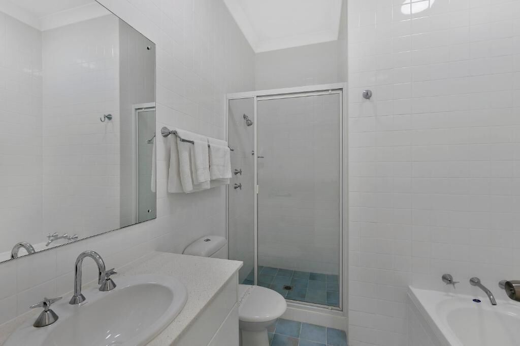 A modern bathroom with a large mirror, two sinks, a toilet, and a glass-enclosed shower.