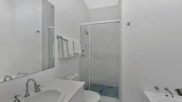 A modern bathroom with a large mirror, two sinks, a toilet, and a glass-enclosed shower.
