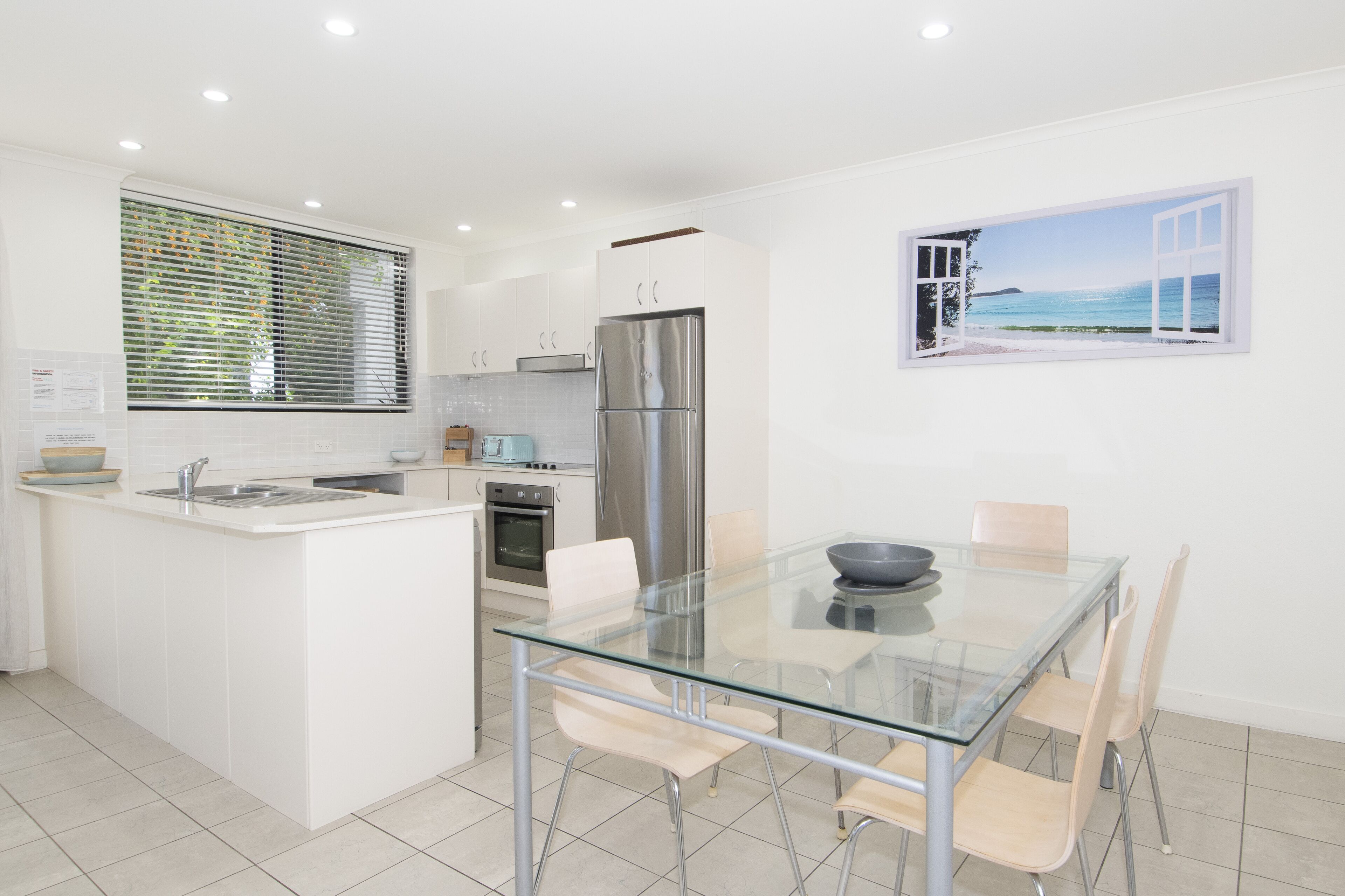 A modern kitchen with a central island, stainless steel appliances, and a dining area with a glass table and chairs.