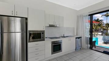 A modern kitchen with stainless steel appliances, white cabinetry, and a view of a pool through a glass door.