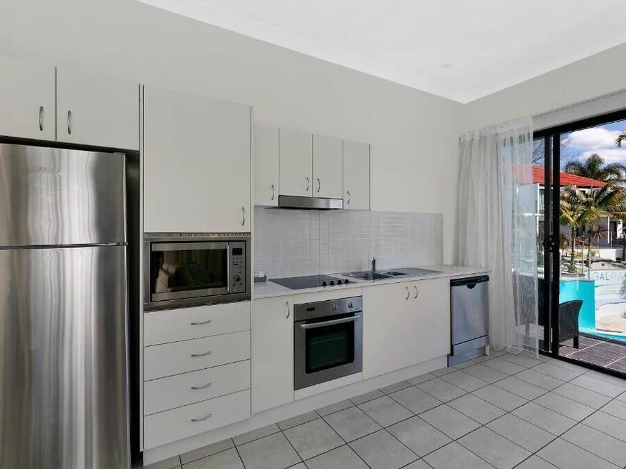 A modern kitchen with stainless steel appliances, white cabinetry, and a view of a pool through a glass door.