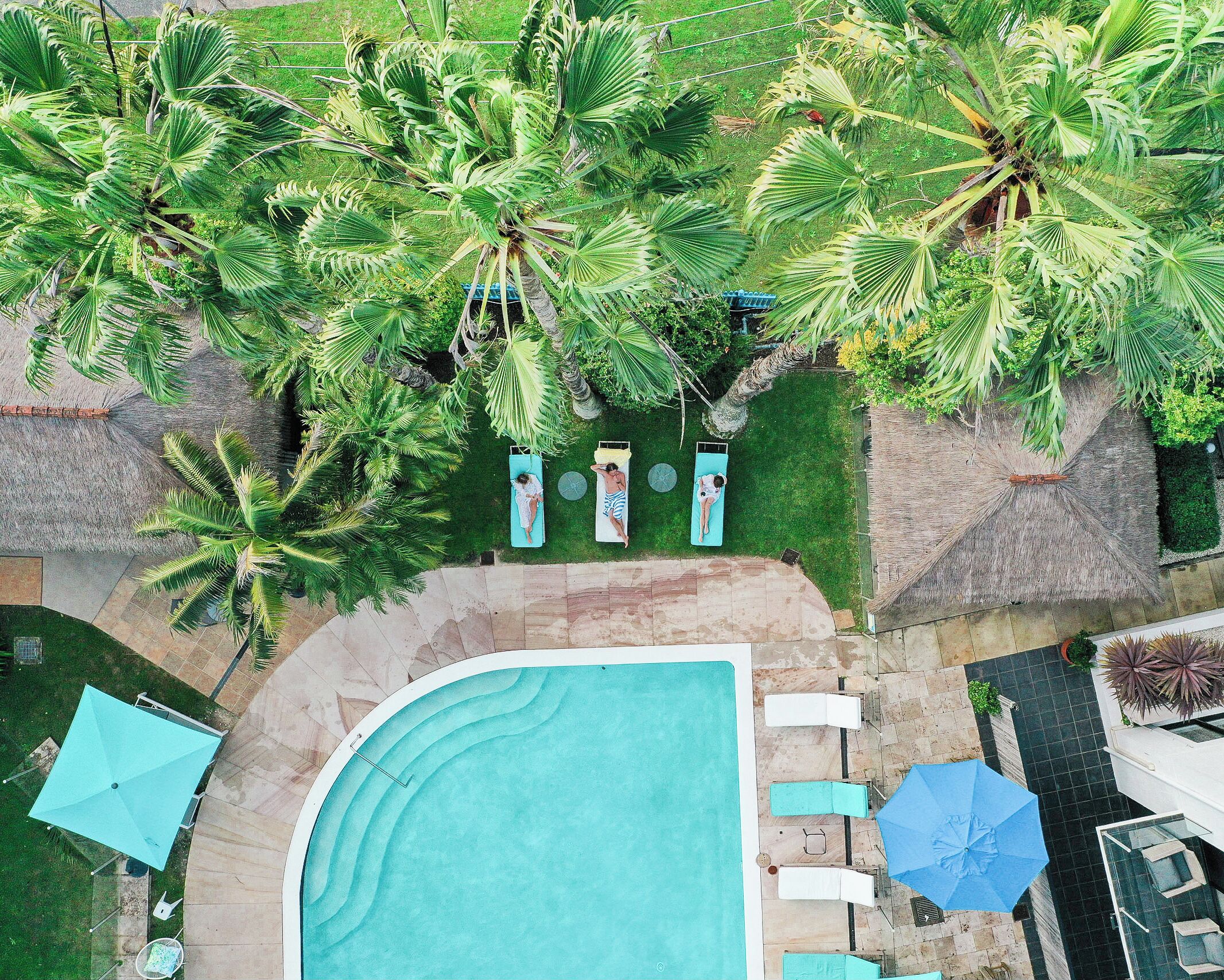 An aerial view of a pool area with lounge chairs, umbrellas, and palm trees.