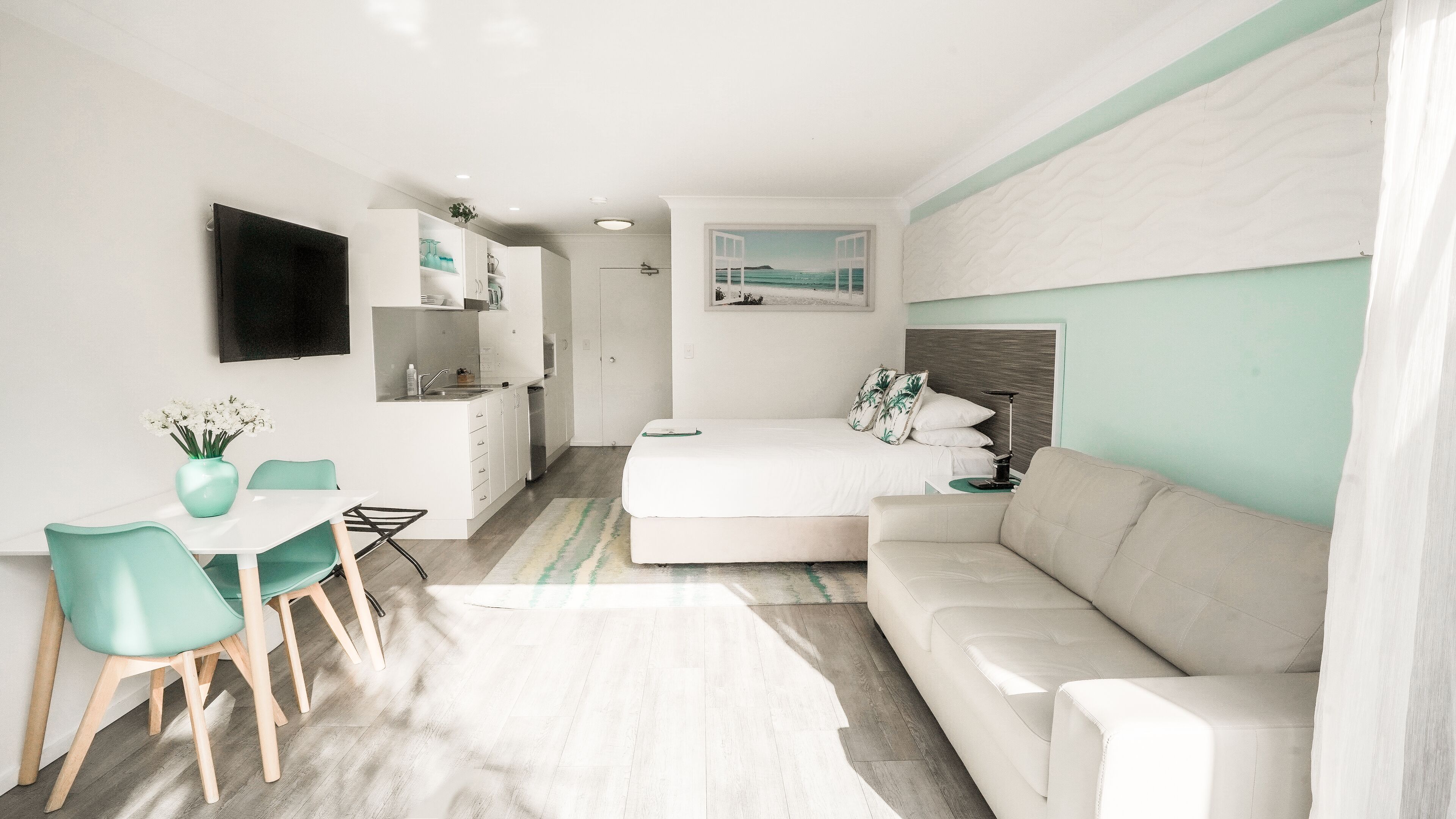 A compact living space with a kitchenette, a dining area with a table and chairs, a bed with a headboard, and a large window with a view.