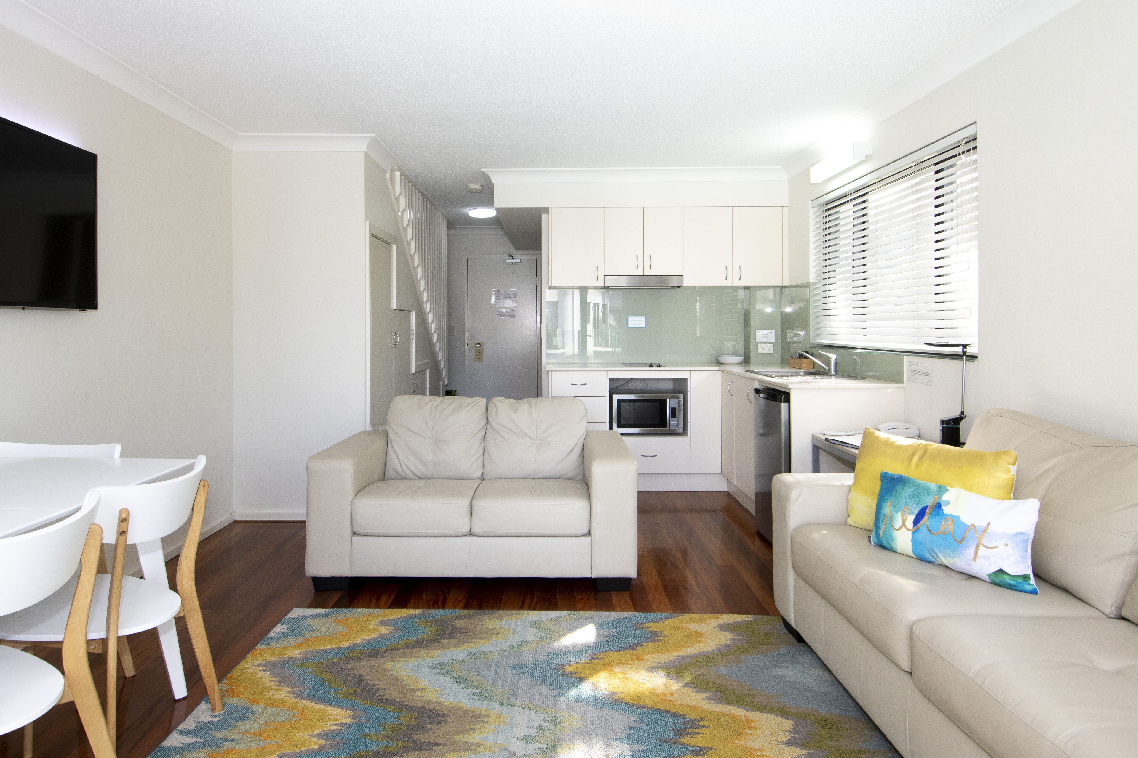 Una sala de estar moderna con un sofá, una mesa de comedor con sillas y una zona de cocina con armarios y electrodomésticos.