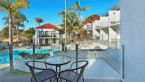 Un hotel moderno con piscina, palmeras y un cielo azul despejado.