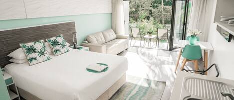 A modern hotel room with a large bed, a sofa, a dining area with a table and chairs, and a view of the outdoors.