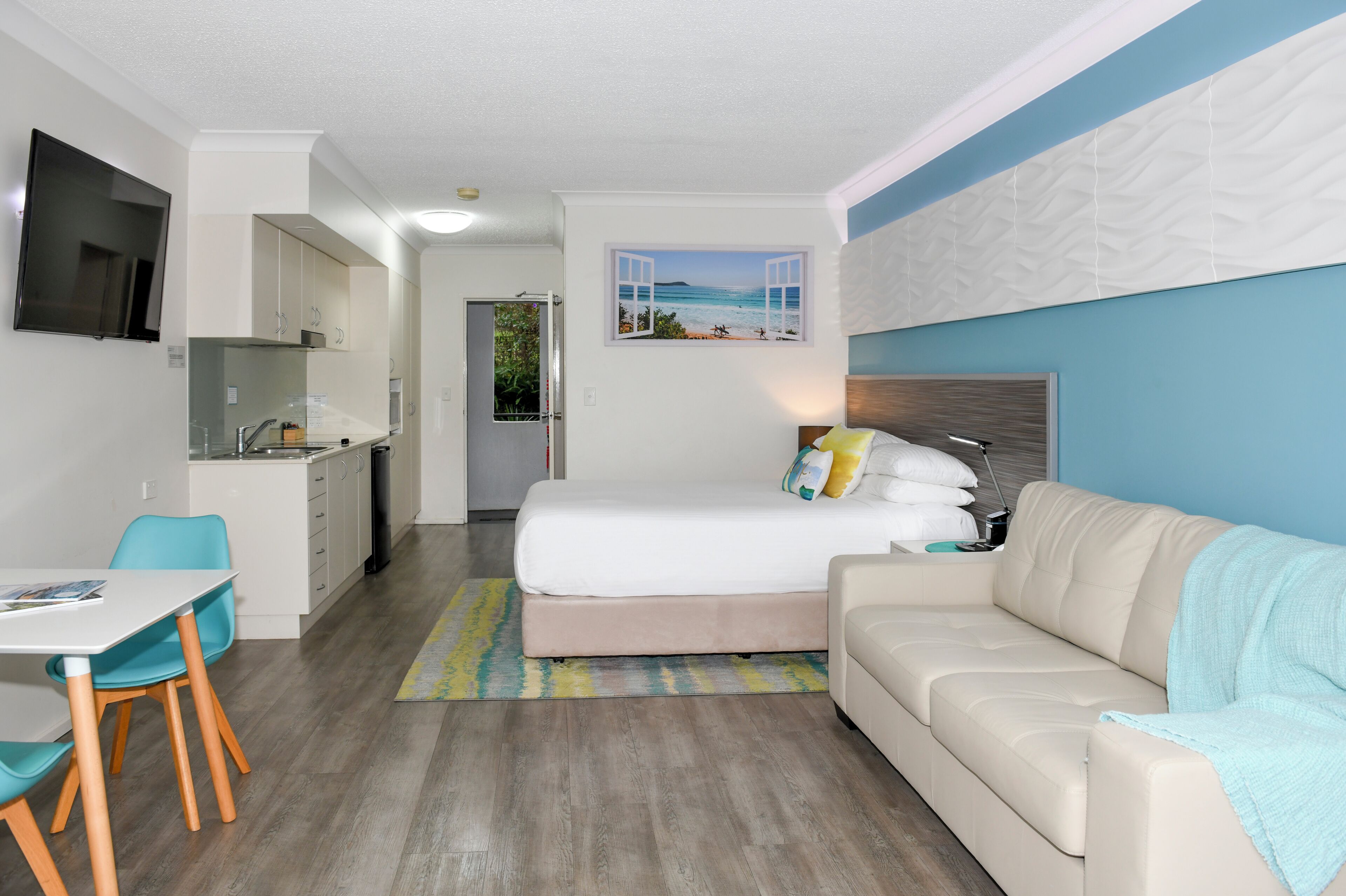 A compact hotel room with a bed, a sofa, a dining area, and a kitchenette.