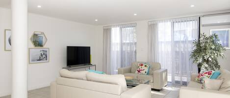 A modern living room with a flat-screen TV, two sofas, a coffee table, and a large potted plant.