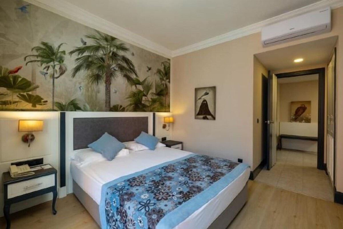 A hotel room with a bed, nightstands, a wall mural, and an air conditioning unit.