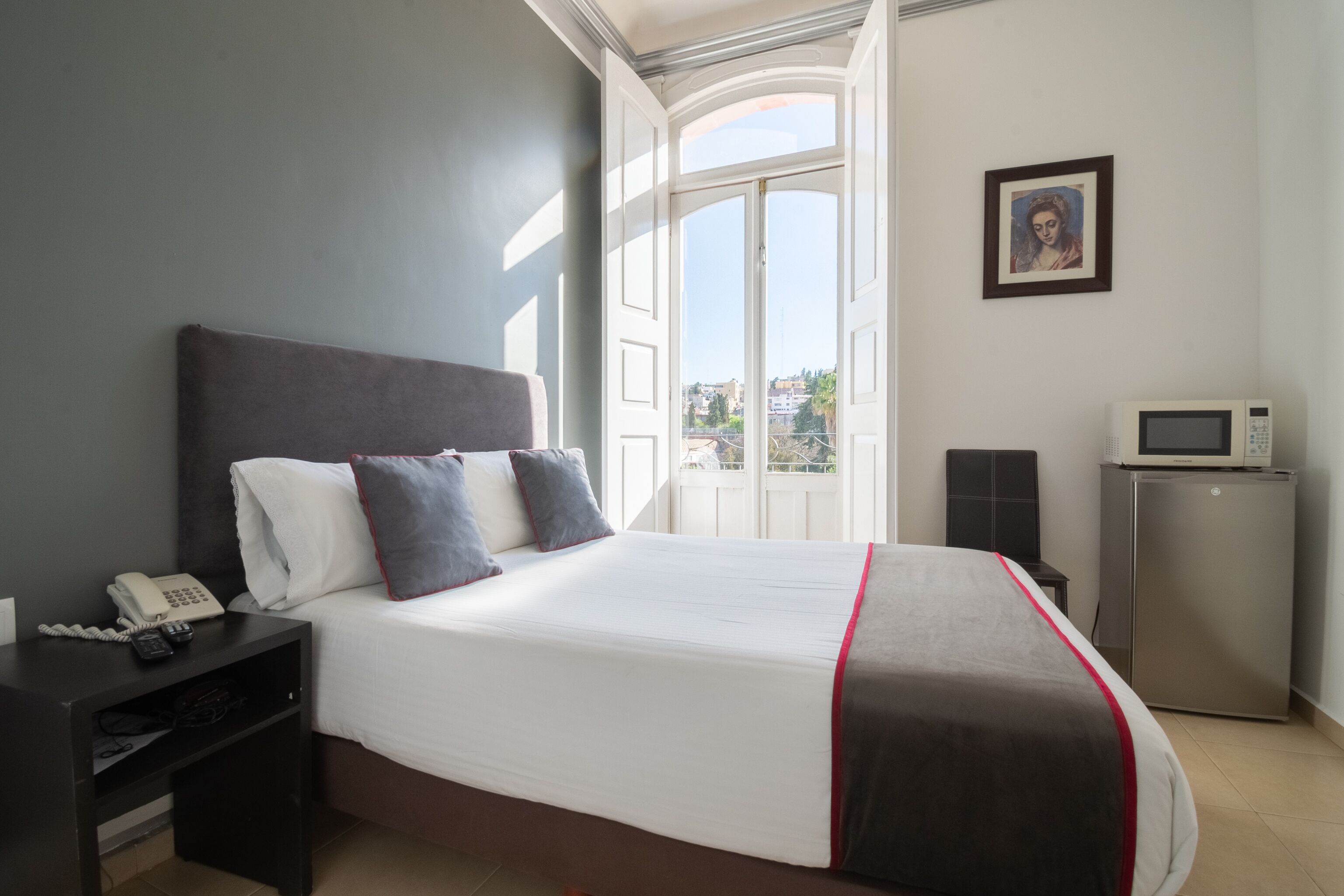 A hotel room with a large bed, a bedside telephone, a small refrigerator, and a picture on the wall.