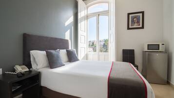 A hotel room with a large bed, a bedside telephone, a small refrigerator, and a picture on the wall.
