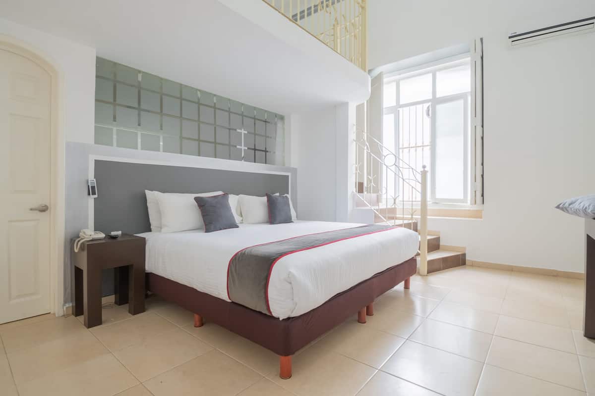 A modern bedroom with a large bed, a bedside table, a small table with a phone, a window with a view, and a staircase.