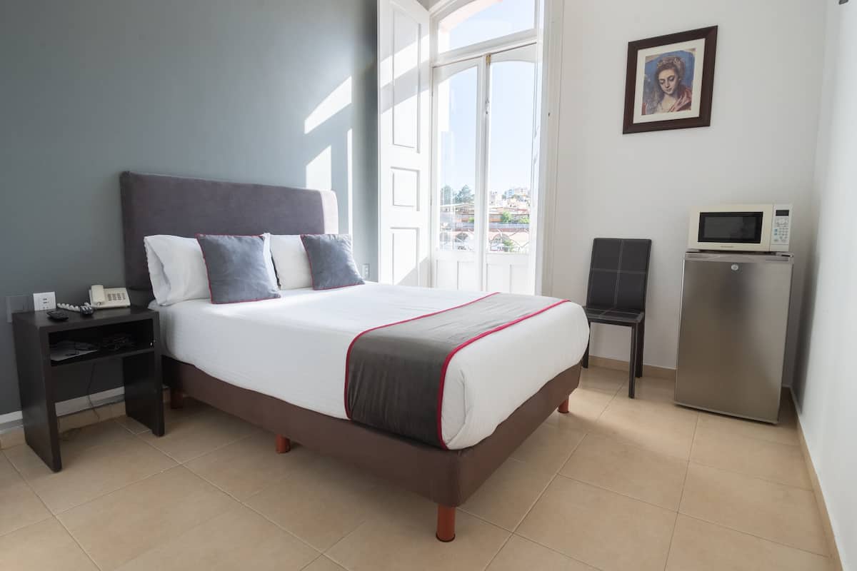A neatly arranged bedroom with a bed, bedside table, and a small desk with a microwave.