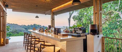 A bar area with a wooden ceiling, bar stools, and a view of the forest.