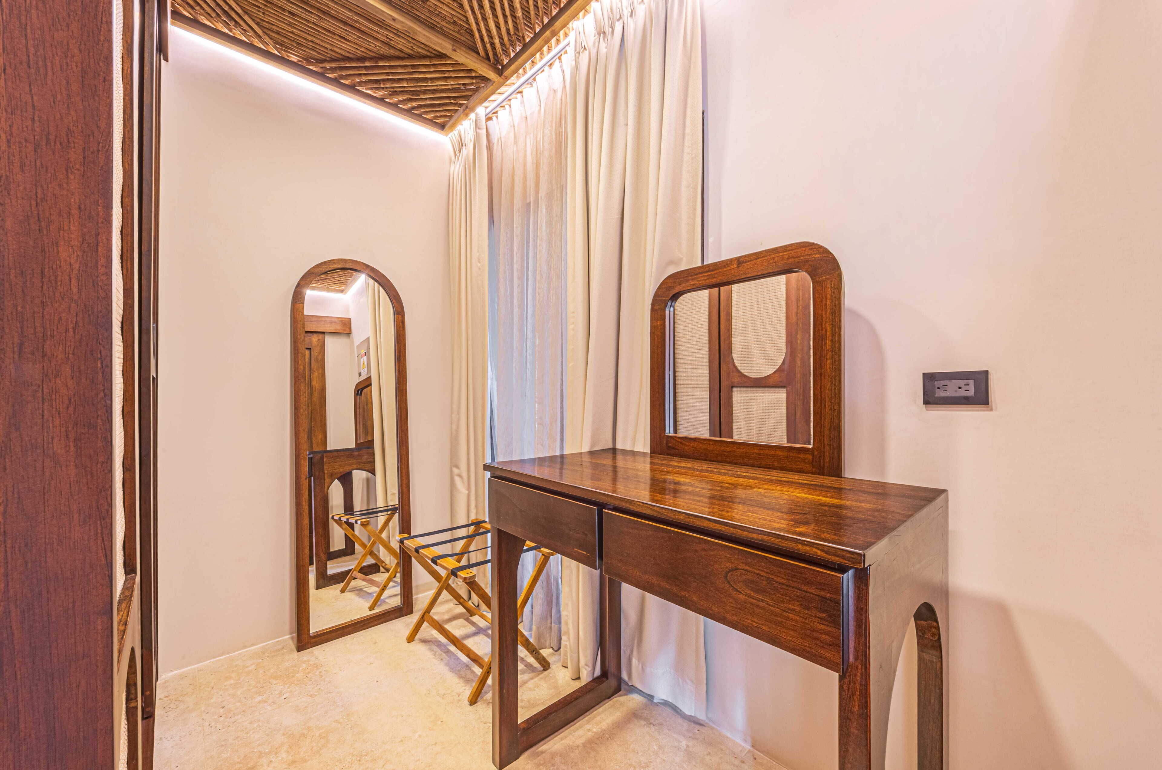A room with a wooden desk, a mirror, a folding chair, and a ceiling with a wooden pattern.