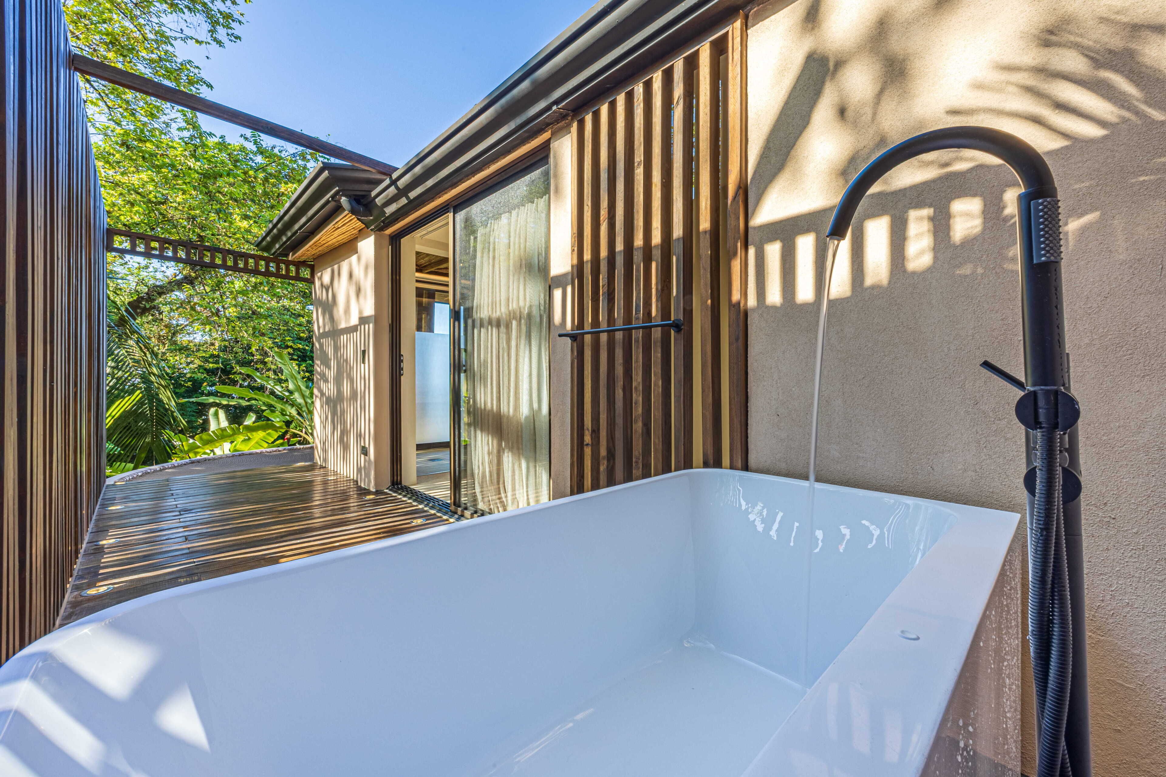 A modern outdoor bathtub with a hose, surrounded by wooden deck and large windows.