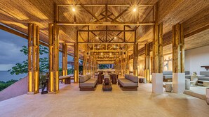 A spacious lounge area with wooden beams, seating arrangements, and a view of the ocean. - Tiki Villas Rainforest Lodge & Spa (Bahía Ballena)