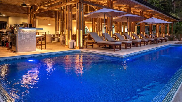 A poolside area with lounge chairs and umbrellas, a bar area, and a view of the pool. - Tiki Villas Rainforest Lodge & Spa (Bahía Ballena)
