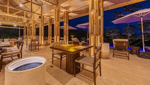 An outdoor dining area with wooden tables and chairs, a large water feature, and umbrellas. - Tiki Villas Rainforest Lodge & Spa (Bahía Ballena)