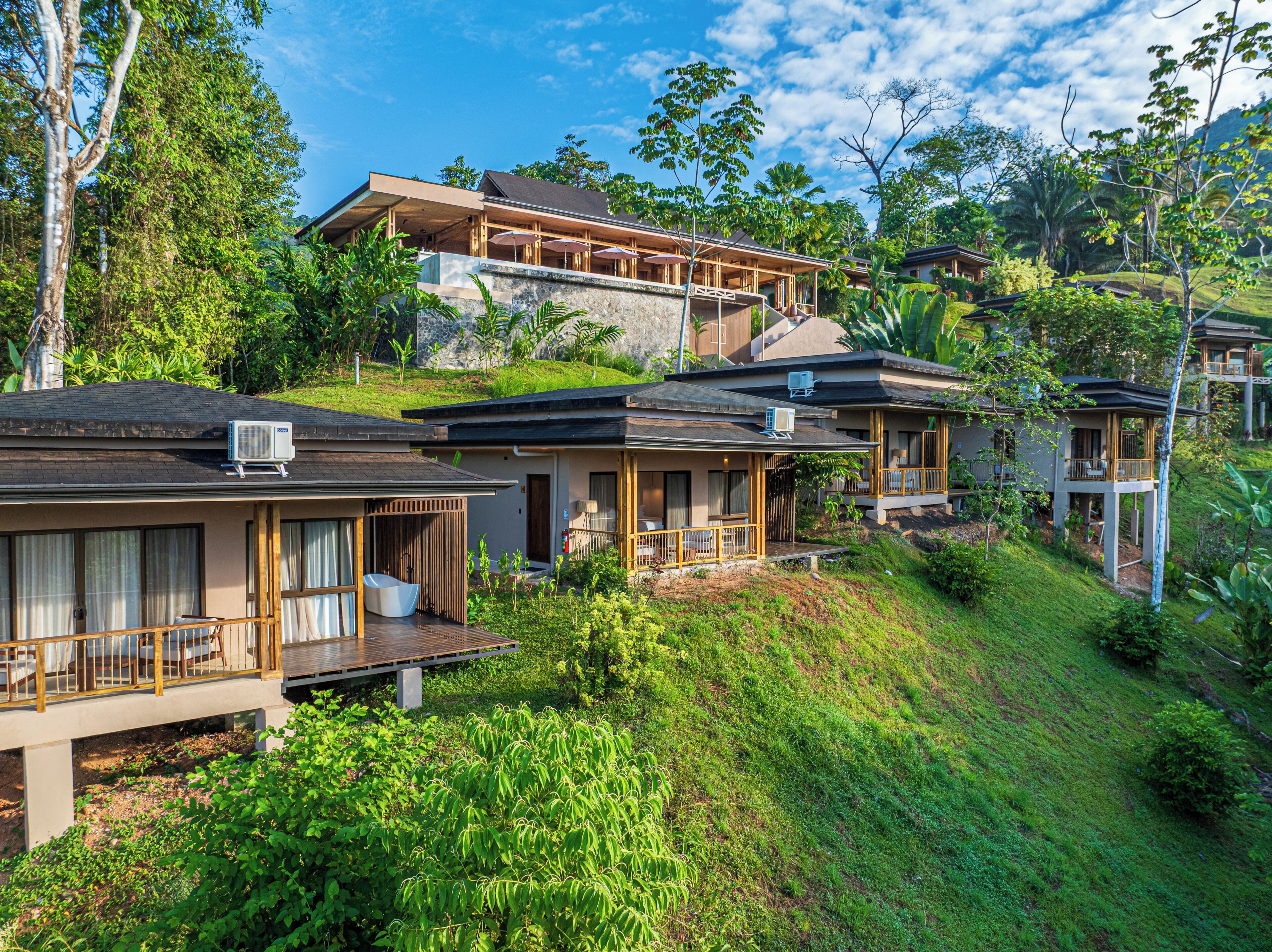 Een resort met meerdere gastvrije villa's, elk met een balkon, een zwembad en uitzicht op de omliggende groene omgeving.