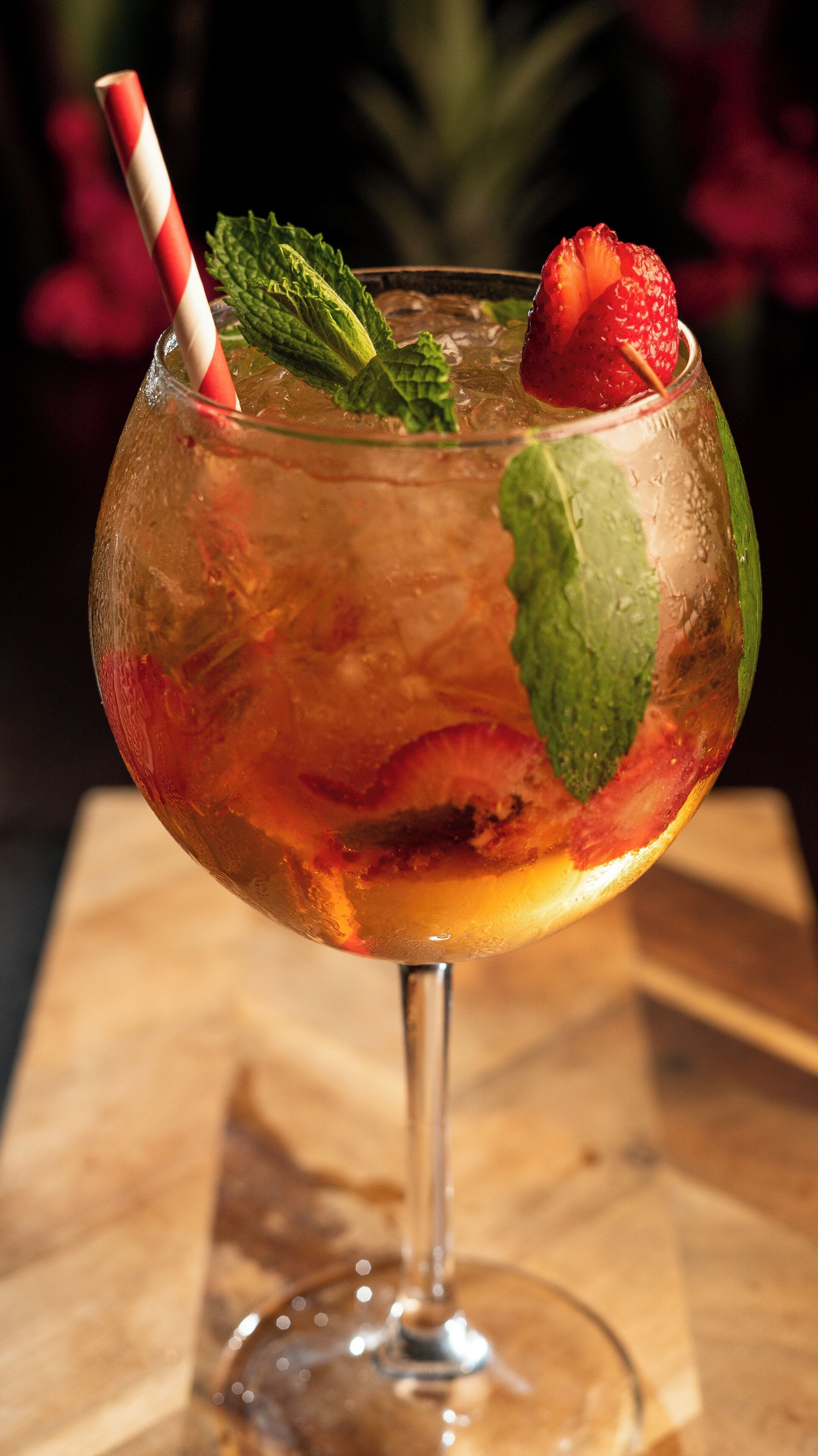 A cocktail glass with a straw, mint leaves, and a strawberry.