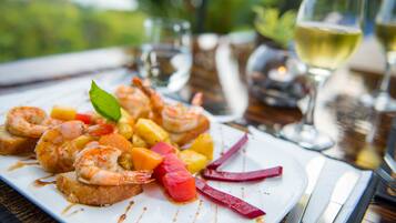 Un plato de camarones y fruta sobre una mesa, con una copa de vino blanco y una vela al fondo.
