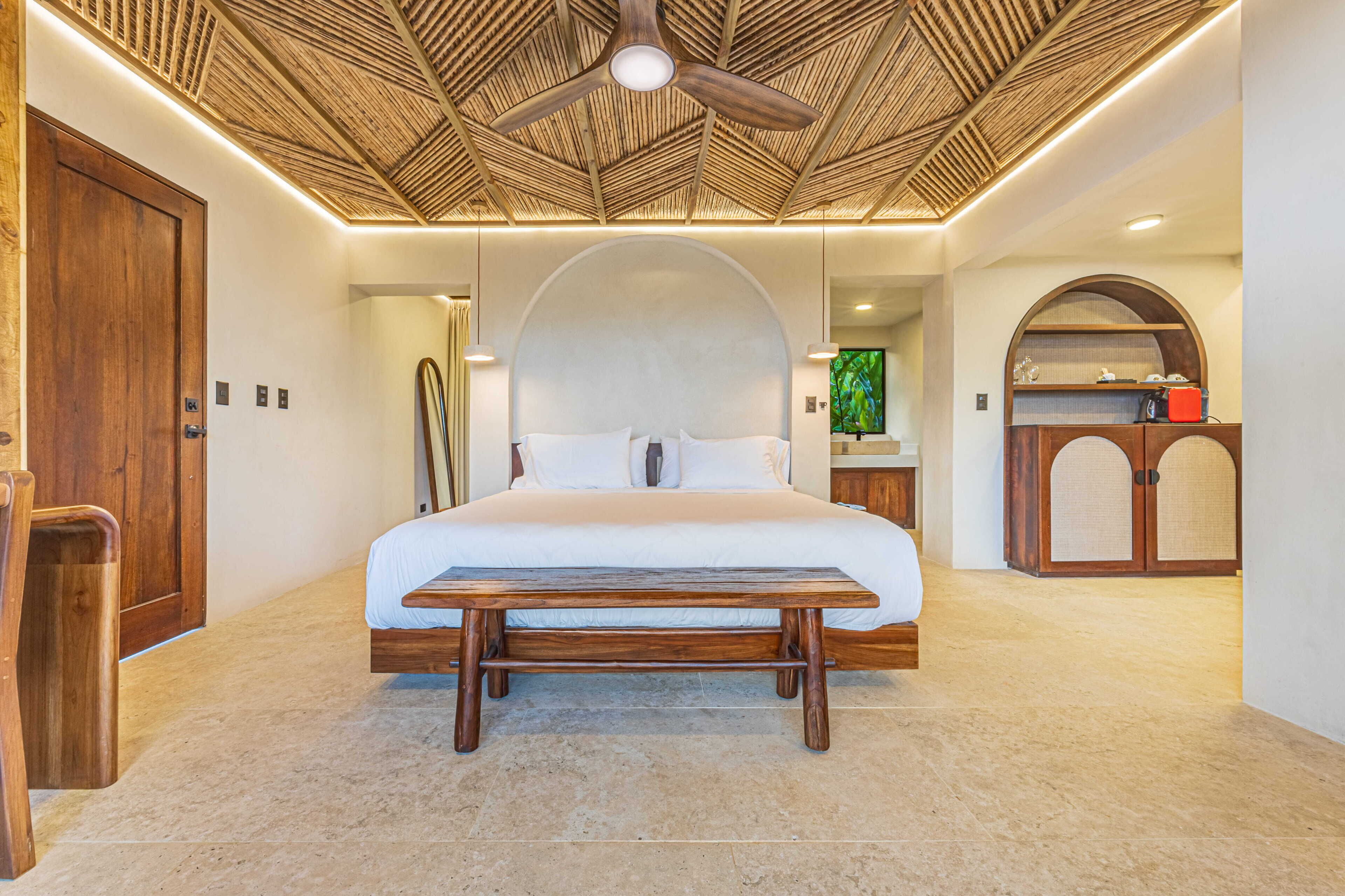 A bedroom with a bed, wooden bench, ceiling fan, and a wooden cabinet.