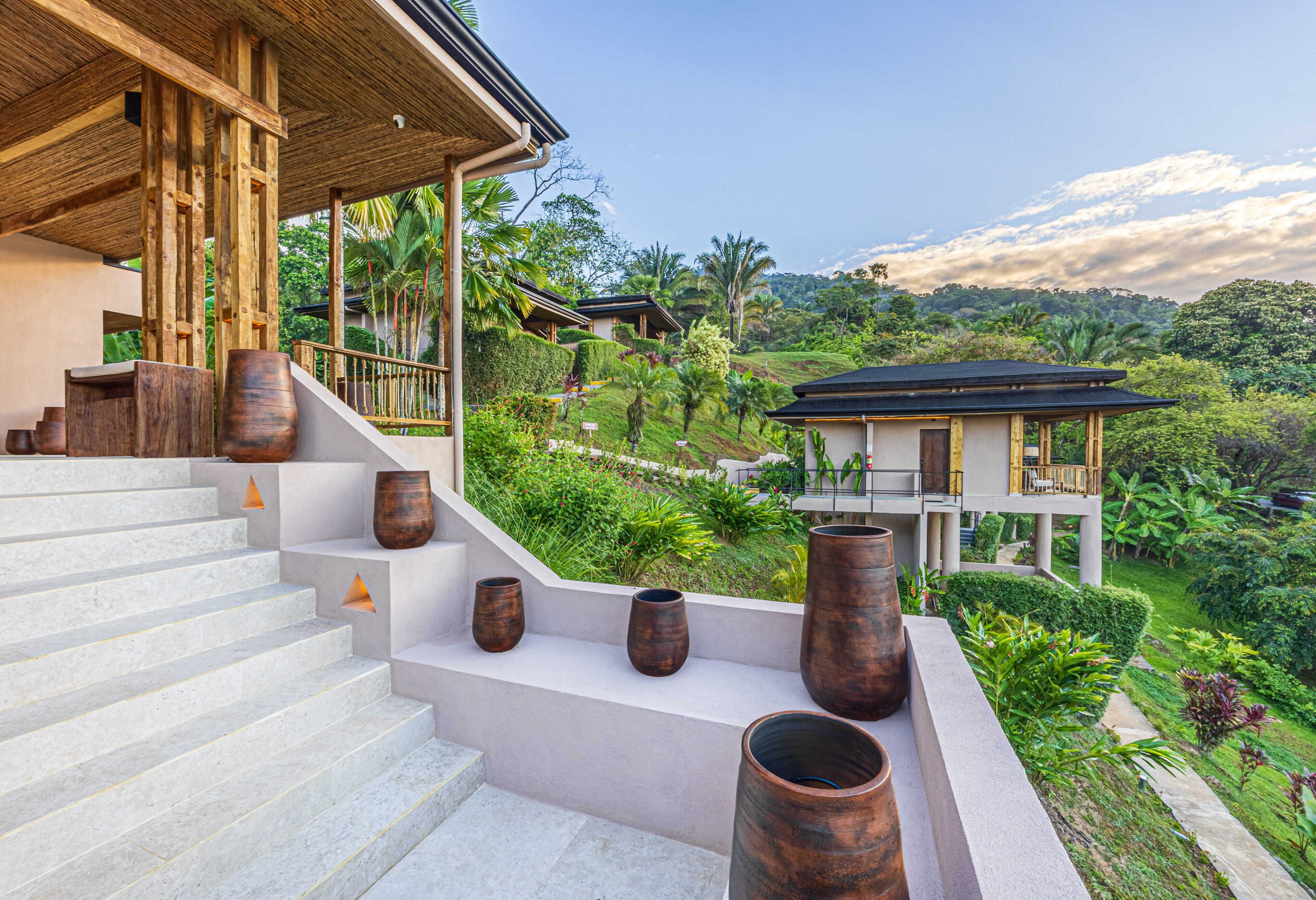 A modern building with a staircase leading to a balcony overlooking lush greenery and a distant hill.