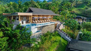 A resort with a pool, lounge chairs, and a view of the surrounding greenery and hills. - Tiki Villas Rainforest Lodge & Spa (Bahía Ballena)