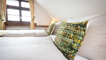 A neatly made bed with white linens and a colorful, textured pillow.
