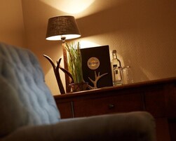 Una mesita de madera con una lámpara, una botella de cerveza Warsteiner, una planta pequeña y un objeto decorativo.