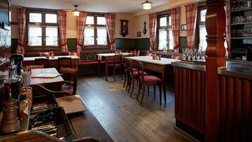 A traditional pub with wooden furniture, a bar area, and red and white checkered curtains.