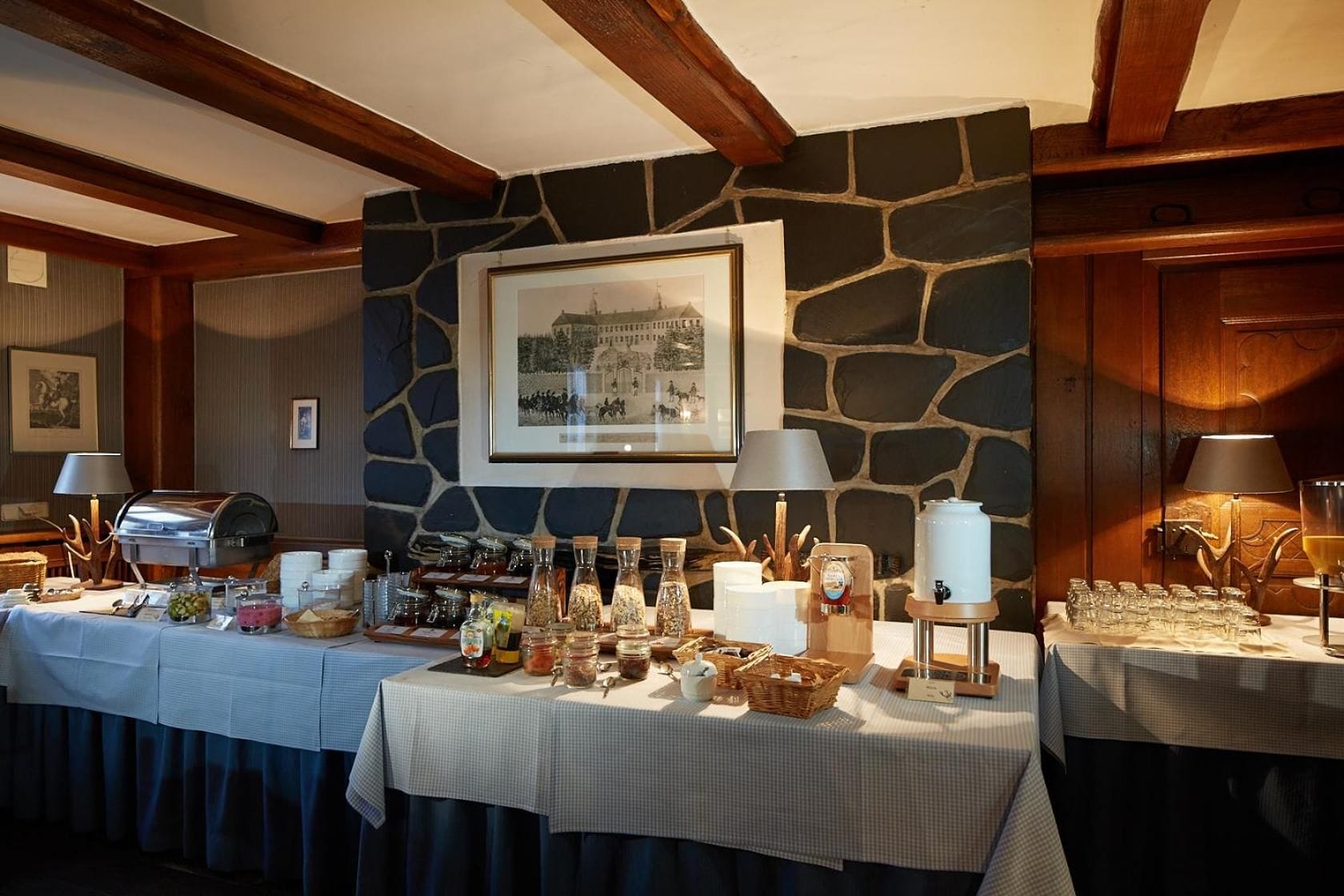 A buffet setup with various food items and a coffee station, set against a stone wall with a framed picture above.