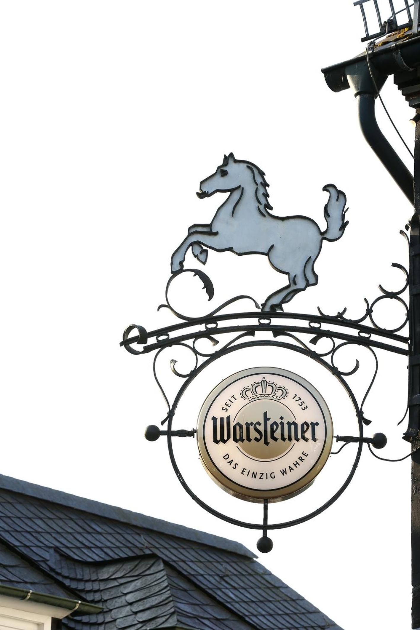 Segno metallico con la sagoma di un cavallo e il nome 'Warsteiner'.