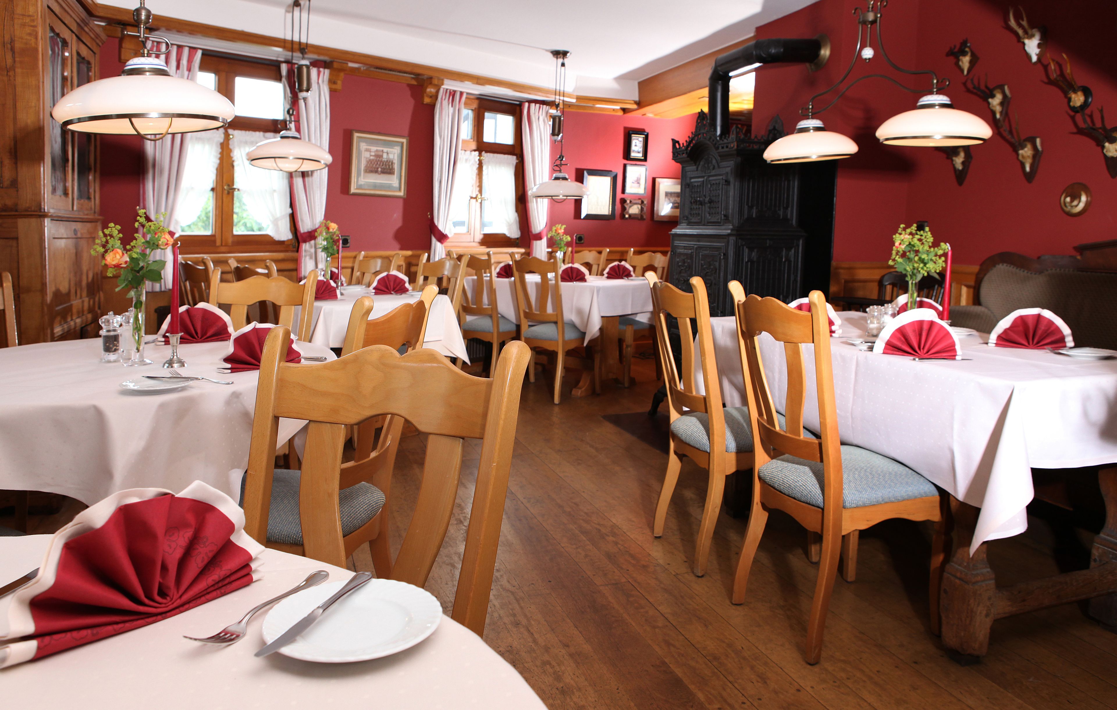 Um restaurante com mesas e cadeiras de madeira, toalhas de mesa vermelhas e brancas, e um fogão preto grande.