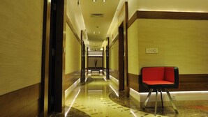 Pasillo de hotel con una silla roja, suelos pulidos e iluminación empotrada.