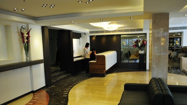 Un vestíbulo de hotel con una mesa de recepción, un sofá negro y un jarrón decorativo con flores.