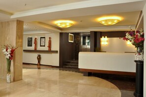 Een hotel receptie met een marmeren vloer, een receptiebalie, een trap en een muur met ingelijste kunstwerken.