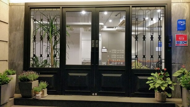 A hotel entrance with a glass door, security signage, and potted plants. - Won's Ville Myeongdong (Seoul)