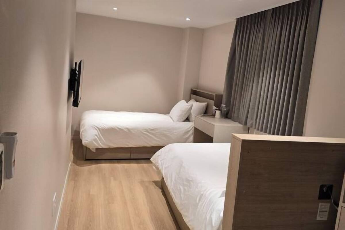 A hotel room with two beds, a wooden headboard, a nightstand, a TV, and a window with curtains.