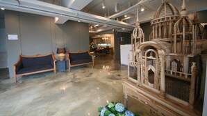 A spacious lobby with a polished concrete floor, a large ornate wooden structure resembling a birdcage, and two dark-colored sofas. - Won's Ville Myeongdong (Seoul)