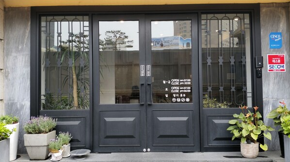 Una puerta doble negra con un panel de vidrio, un letrero de seguridad y una planta a la derecha.